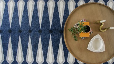 Coffee table, with plant, candle holder and books set atop a blue and white-striped rug.